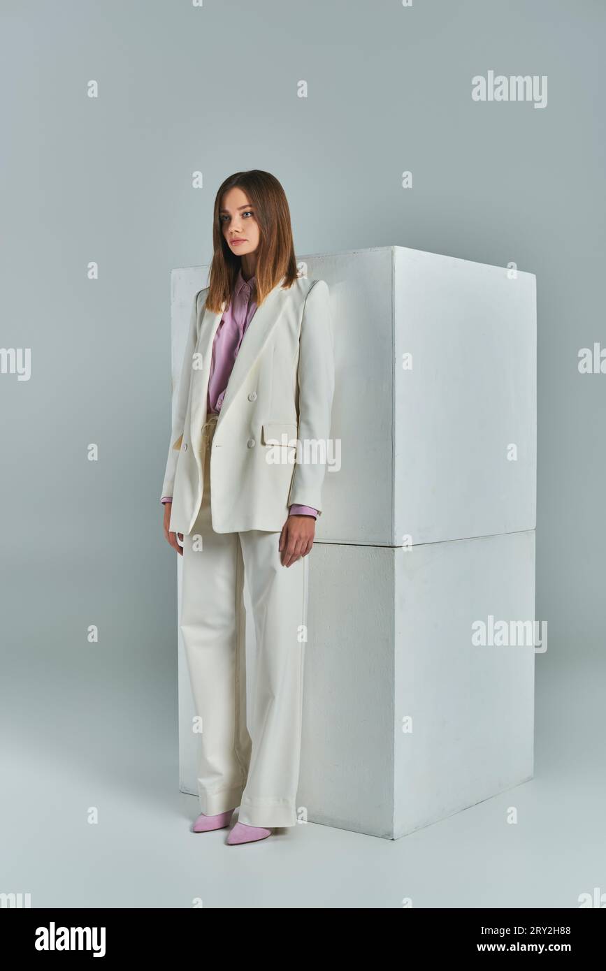 abbigliamento da lavoro alla moda, donna moderna con elegante abito bianco in piedi vicino a cubetti di colore grigio, a lunghezza intera Foto Stock