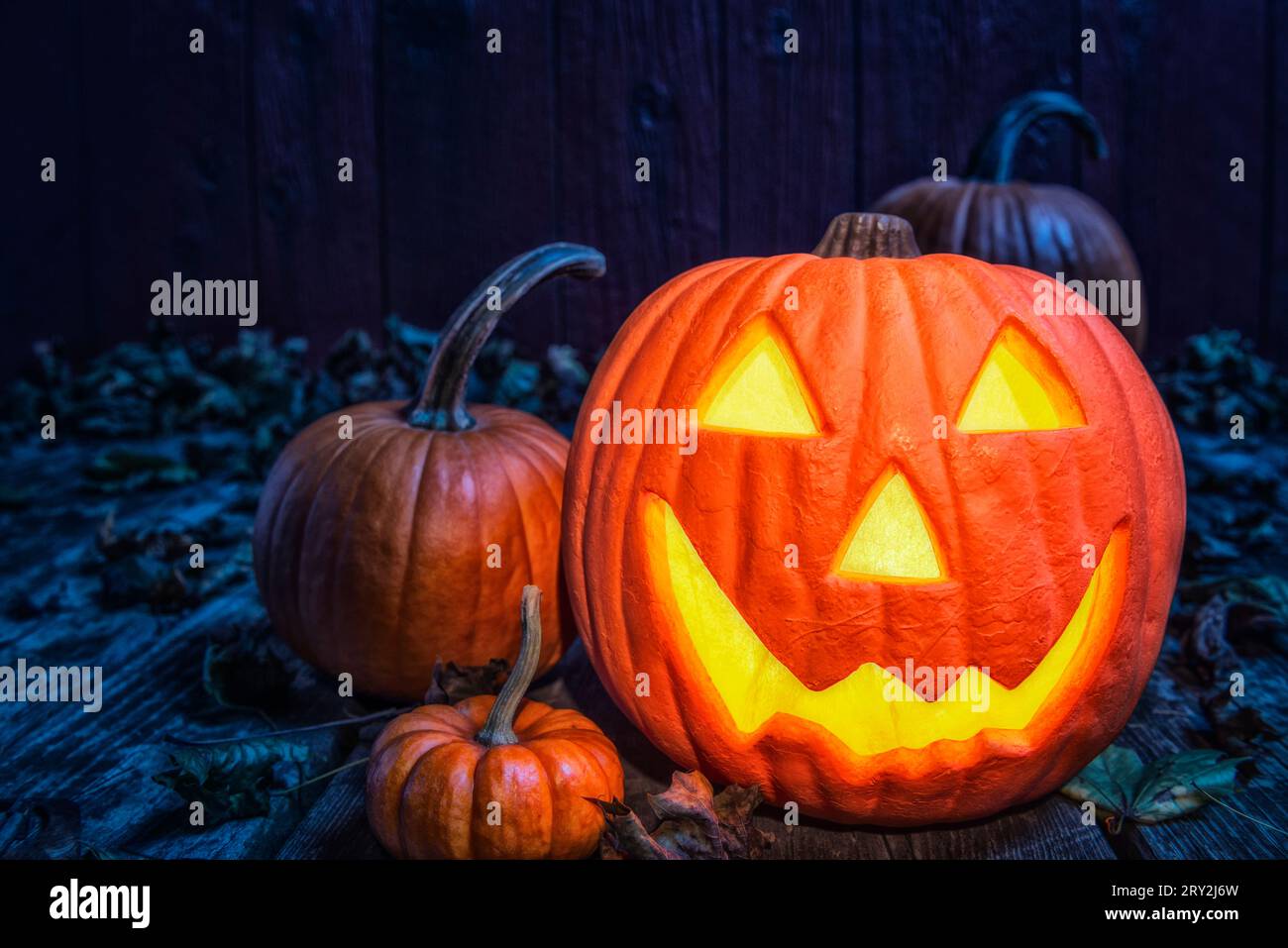 Un primo piano di un sorridente Jack o' Lantern che si crogiolava nella luce blu della luna mentre sedeva su un vecchio ponte di legno intemprato. Foto Stock