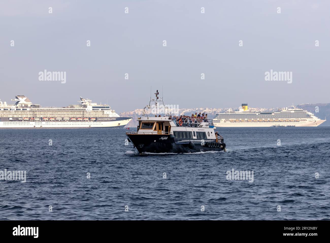 Santorini, Grecia - 7 settembre 2023: Veduta di una piccola barca da escursione che arriva al porto di Athinios Santorini Grecia e due navi da crociera Foto Stock