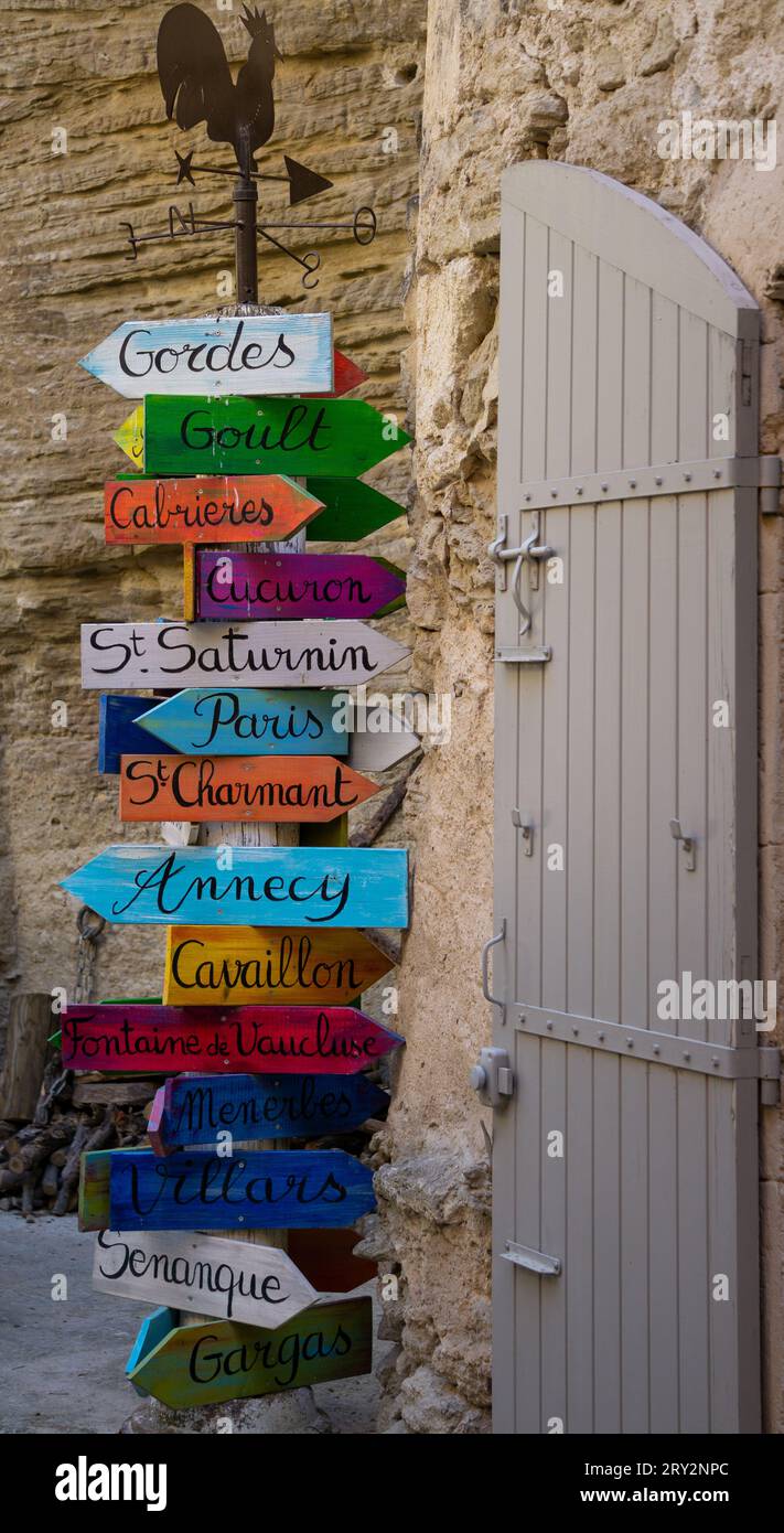 Un vecchio cartello con molte tavole di legno colorate che indicano le destinazioni a sinistra e a destra e sopra è la silhouette di un gallo Foto Stock