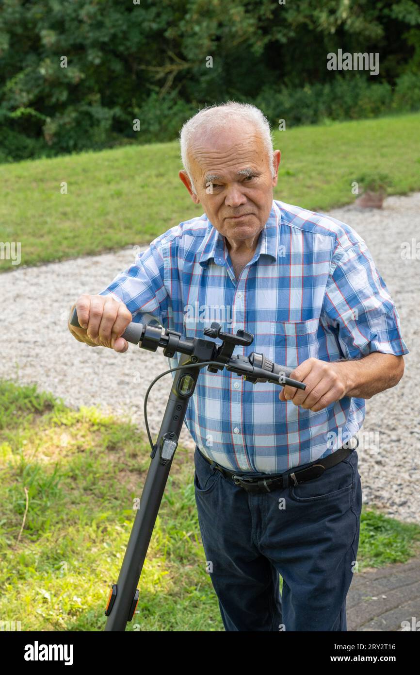 Un uomo anziano che guida con sicurezza un e-scooter, mostrando la combinazione della tecnologia moderna con la grazia dell'età. La sua postura denota esperienza Foto Stock