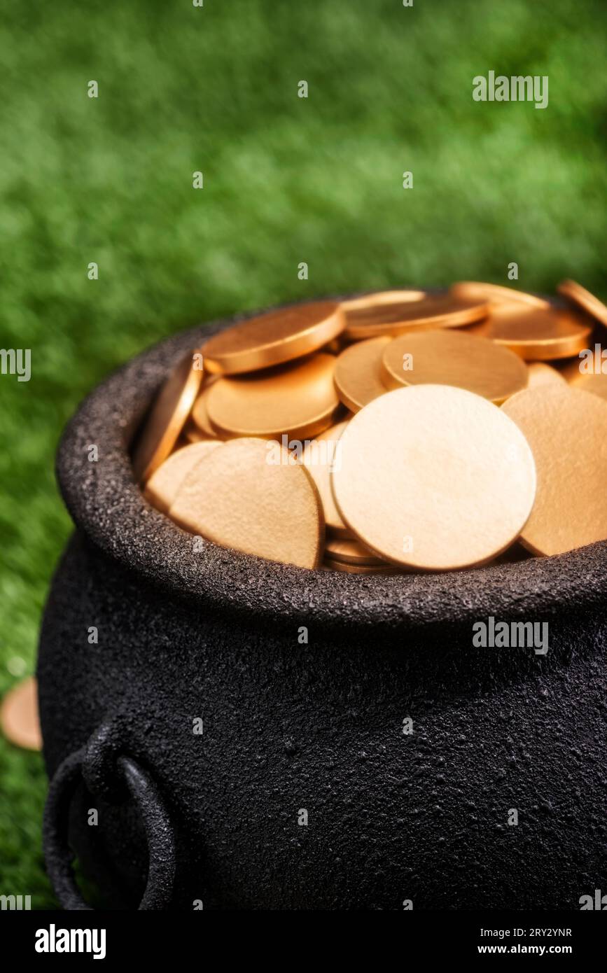Primo piano delle monete d'oro in un bollitore in ferro battuto nero su uno sfondo erboso. Foto Stock