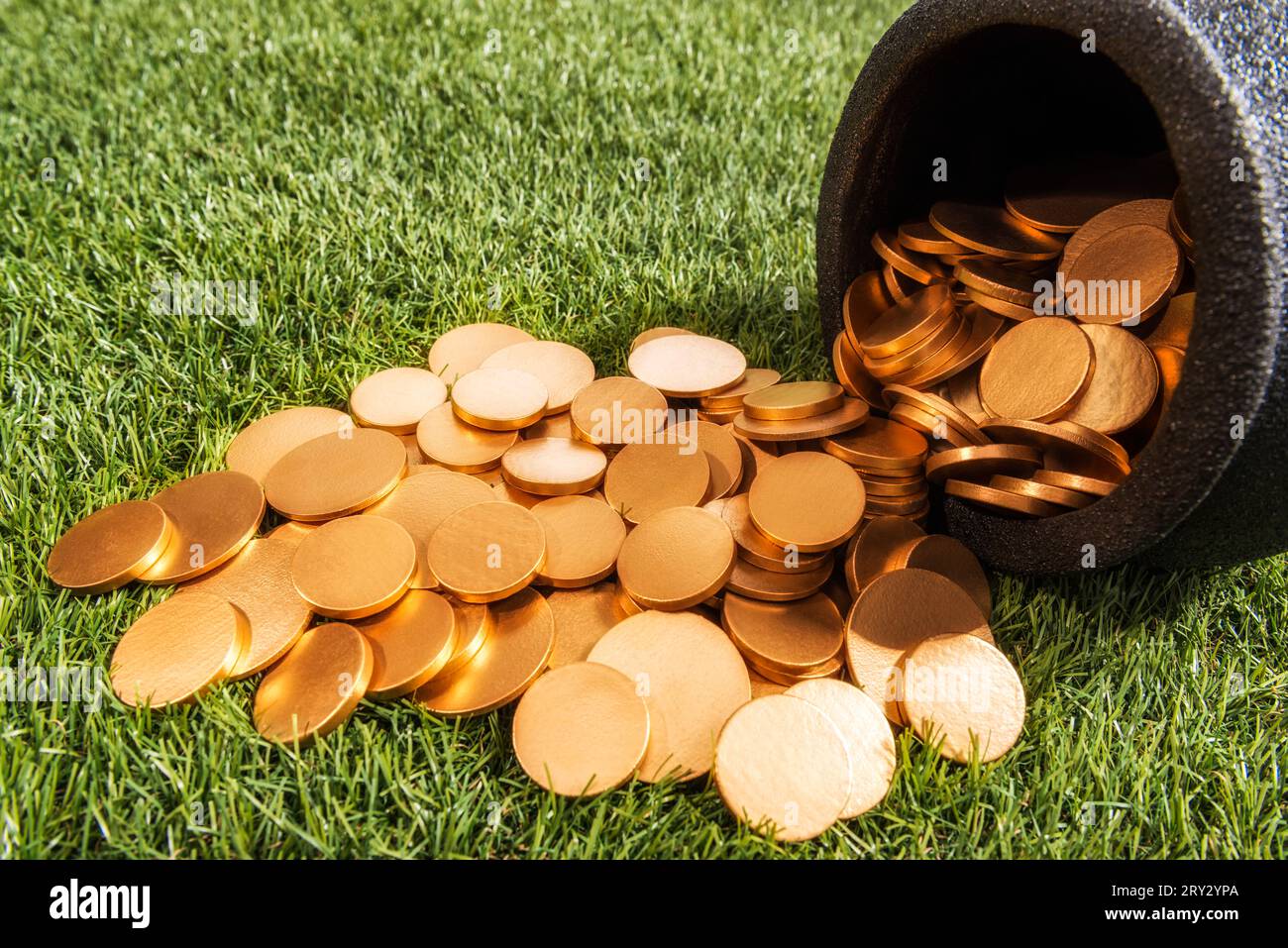 Guardando in basso un bollitore in ferro battuto nero che è stato rovesciato versando le sue monete d'oro sull'erba. Foto Stock