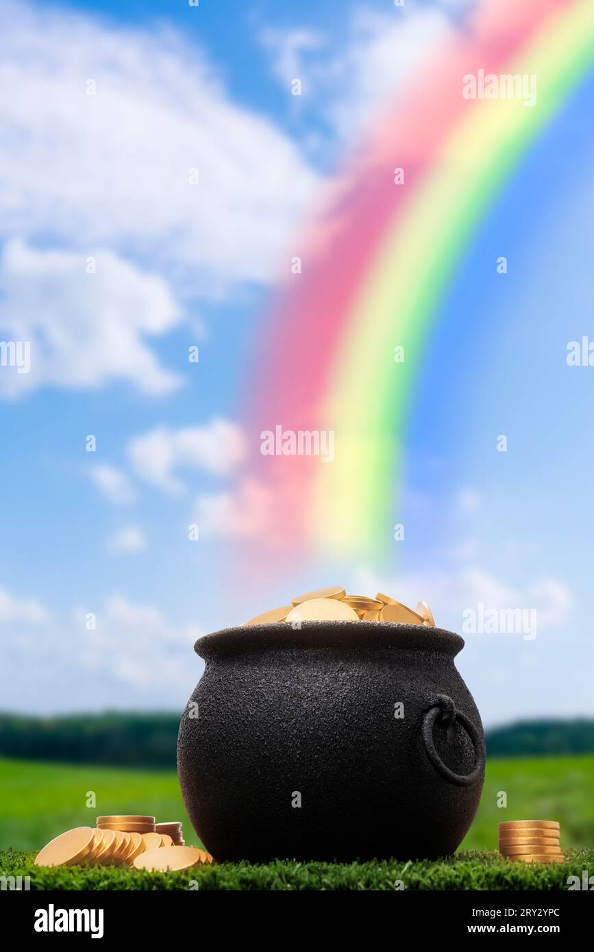 Un vaso di ghisa nera pieno di monete d'oro seduto nell'erba alla fine di un arcobaleno. Alcune monete d'oro sono impilate sull'erba accanto al vaso. Foto Stock