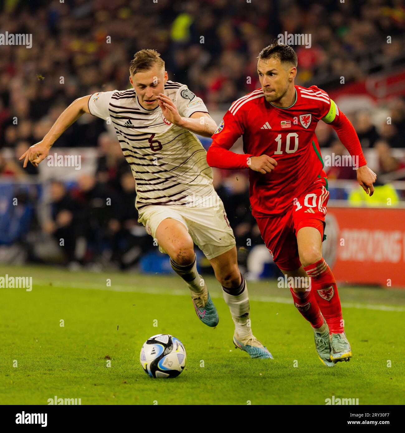 Cardiff, Galles - 28 marzo 2023: Aaron Ramsey sente pressioni da parte della Lettonia Kristers Tobers durante il girone D del Campionato europeo UEFA Foto Stock