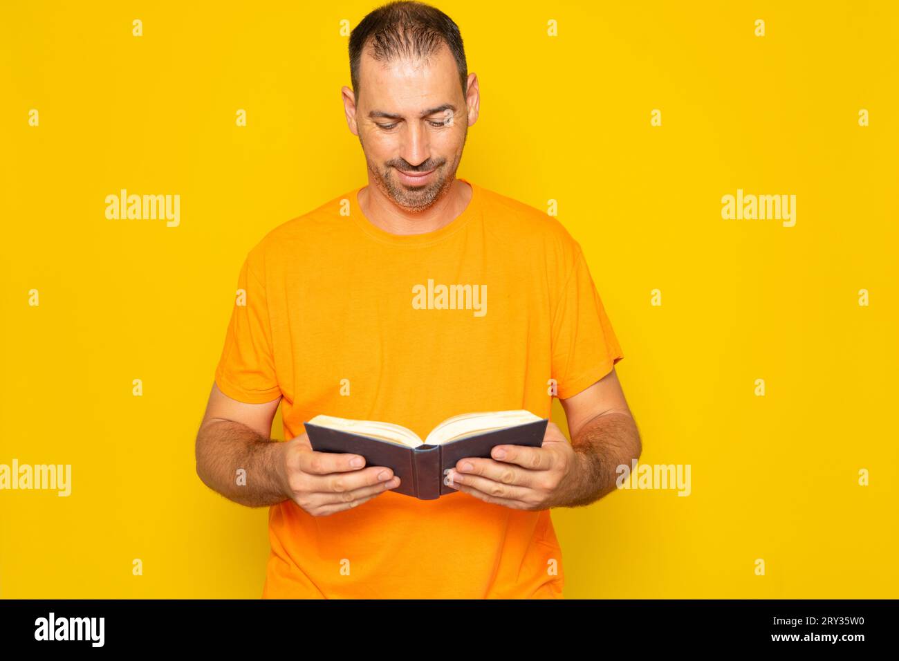 Bearded Hispanic man nei suoi 40 anni, che si allenava con la mente e si divertiva a leggere un libro, isolato sullo sfondo giallo dello studio. Foto Stock