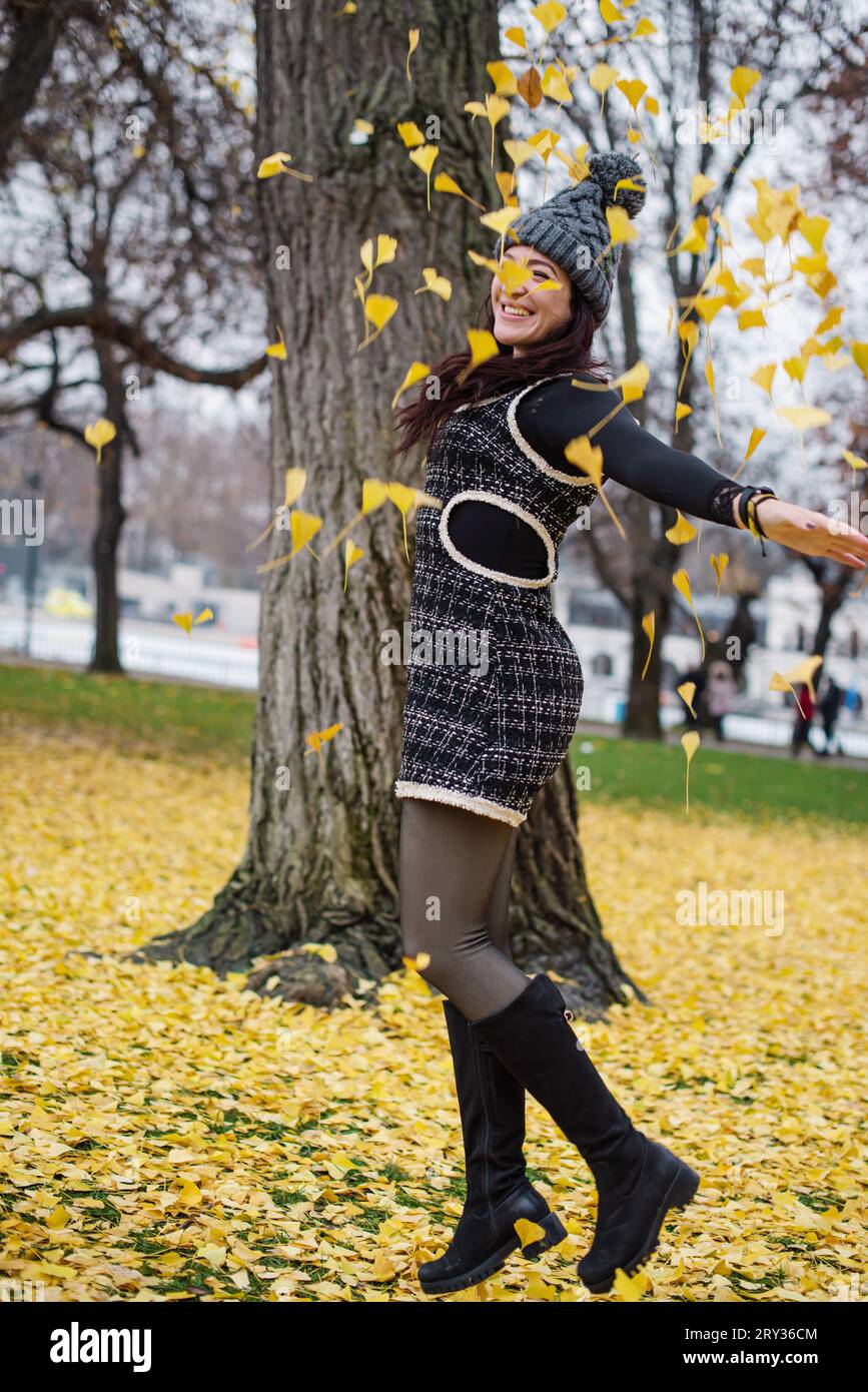 Donna felice che salta in mezzo a una pila di foglie gialle d'autunno. Foto Stock