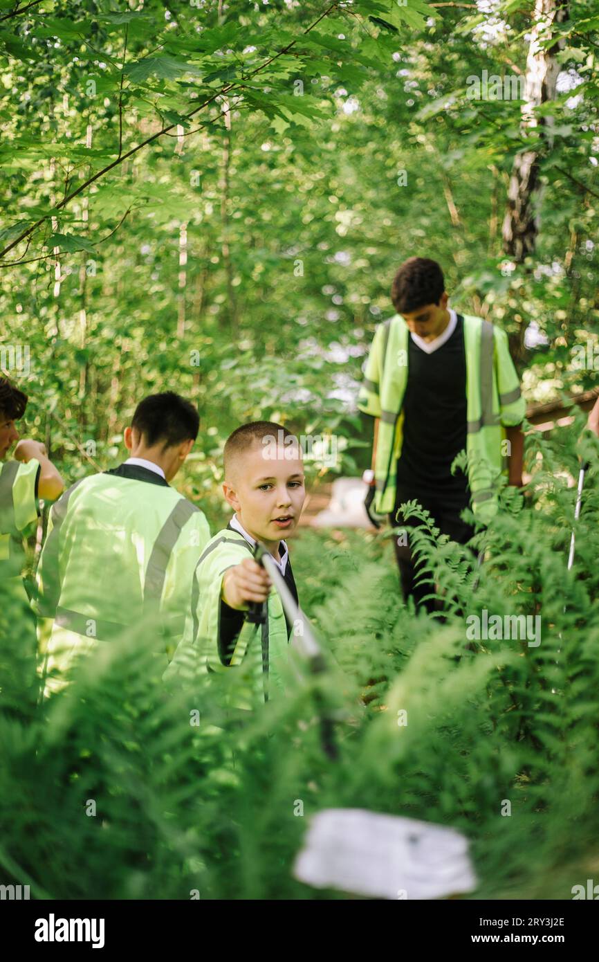 Ragazzo che raccoglie rifiuti di plastica da piante verdi Foto Stock