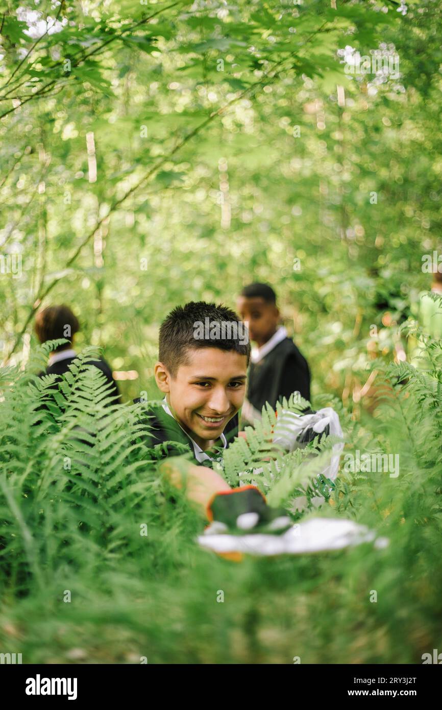 Un ragazzo sorridente che raccoglie la plastica dalla pianta Foto Stock