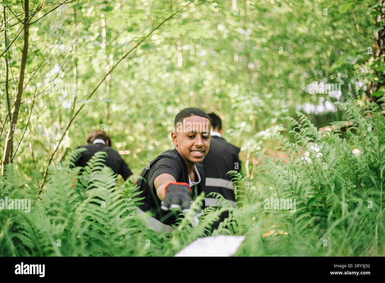 Un adolescente sorridente che raccoglie plastica dalla pianta verde Foto Stock