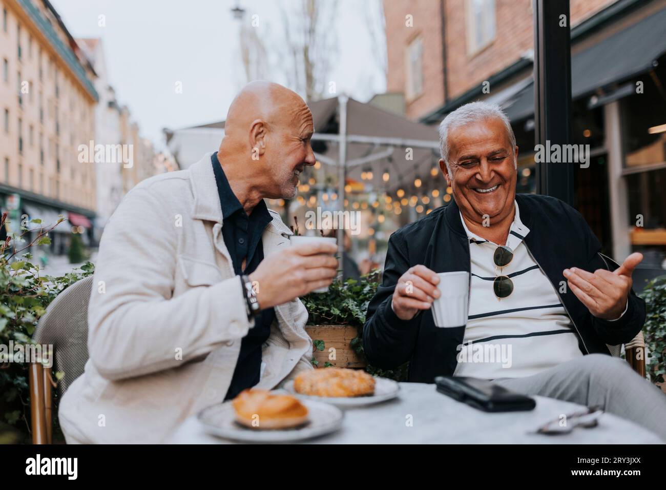 Amici maschi felici che si divertono tra loro mentre bevono un caffè al caffè del marciapiede Foto Stock