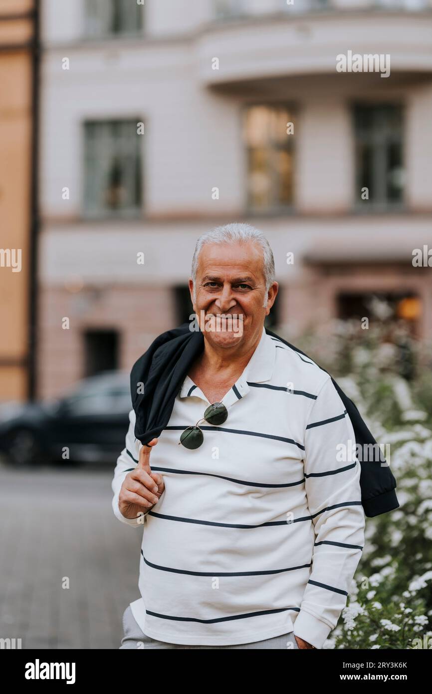 Ritratto di un uomo anziano sorridente con giacca a spalla in piedi per strada Foto Stock