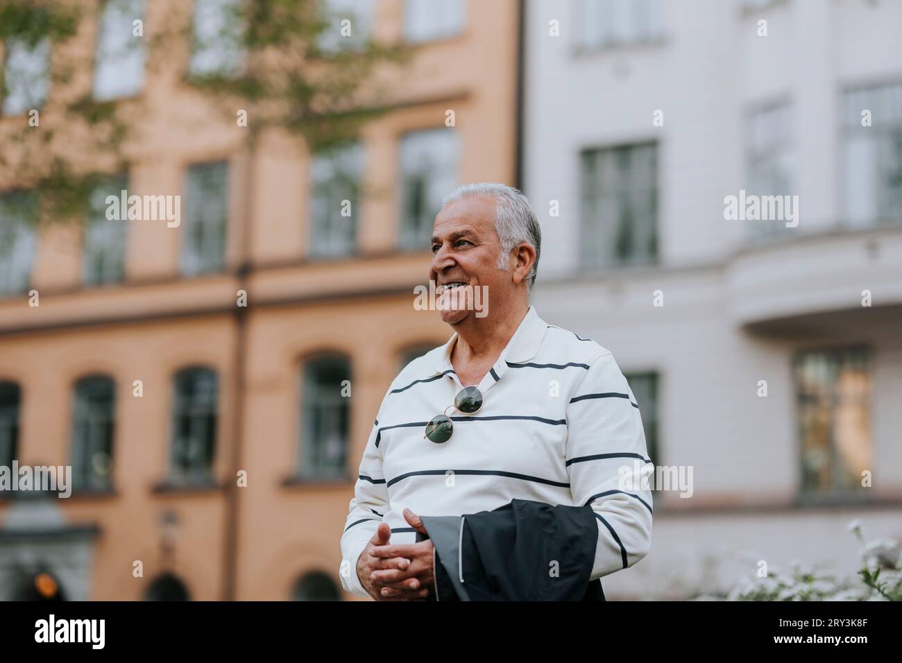 Un anziano sorridente che guarda lontano mentre si trova di fronte all'edificio Foto Stock