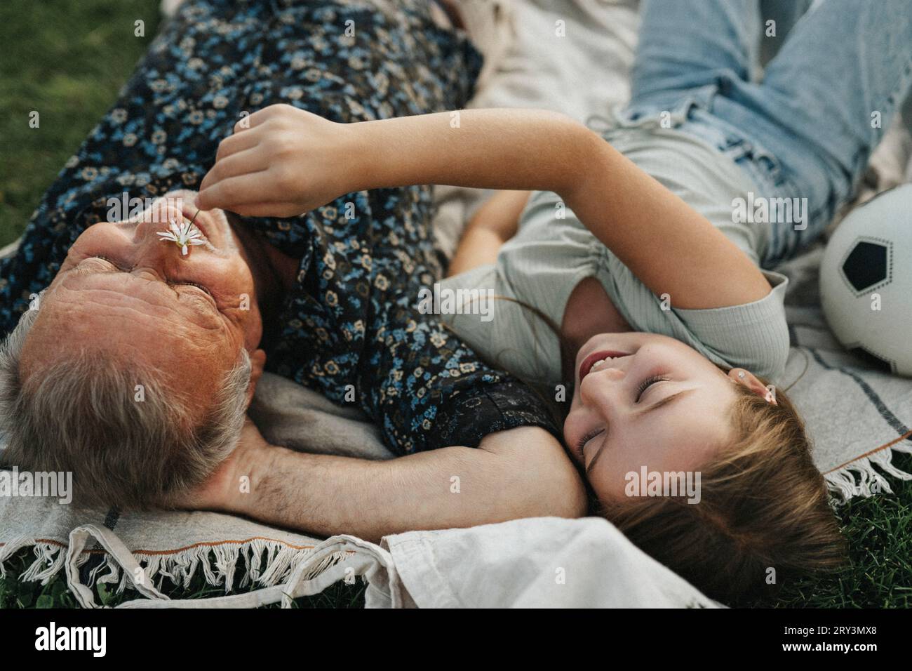 Ragazza sorridente che tiene il fiore sulla faccia del nonno mentre si stende insieme Foto Stock