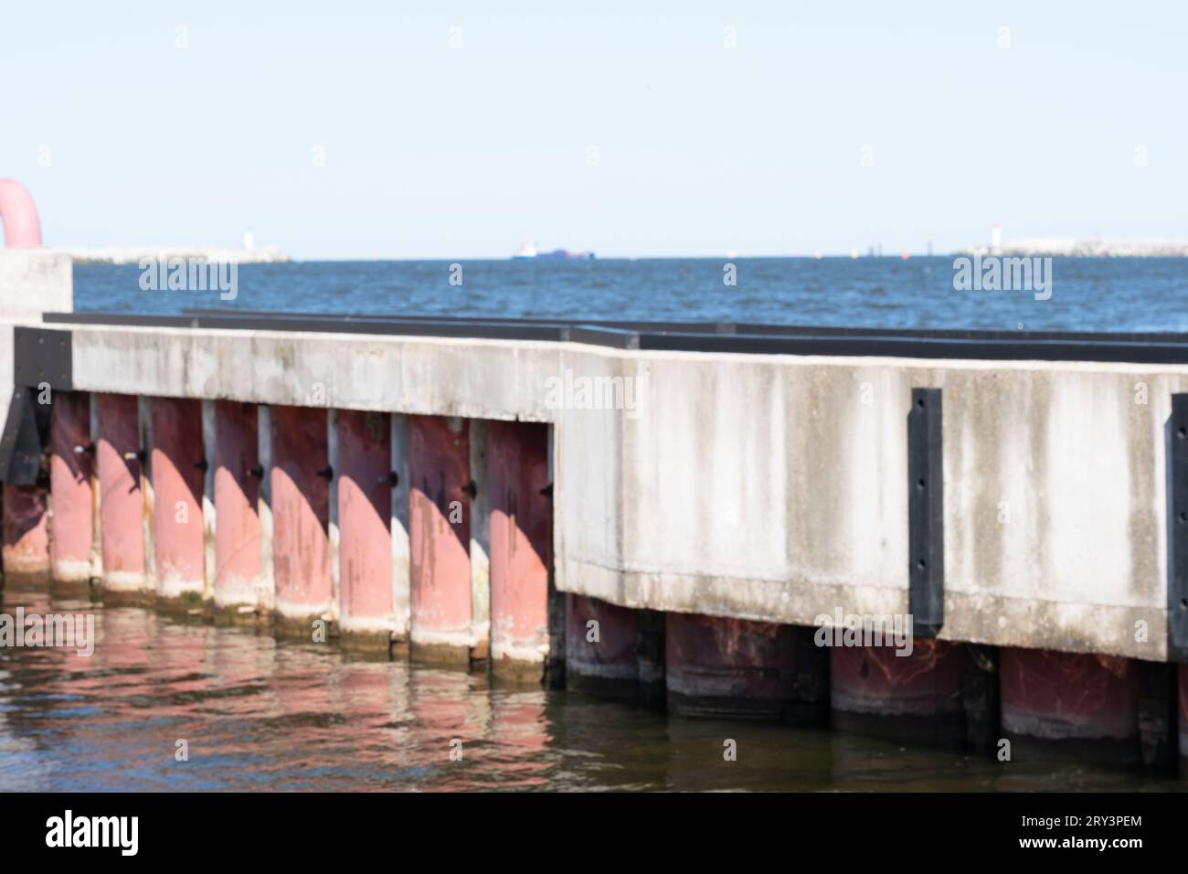Struttura in cemento armato con tubi in metallo rosa nel mare. Cielo limpido, nave e piattaforma galleggiante sullo sfondo. Copia spazio. Background per le virgolette Foto Stock