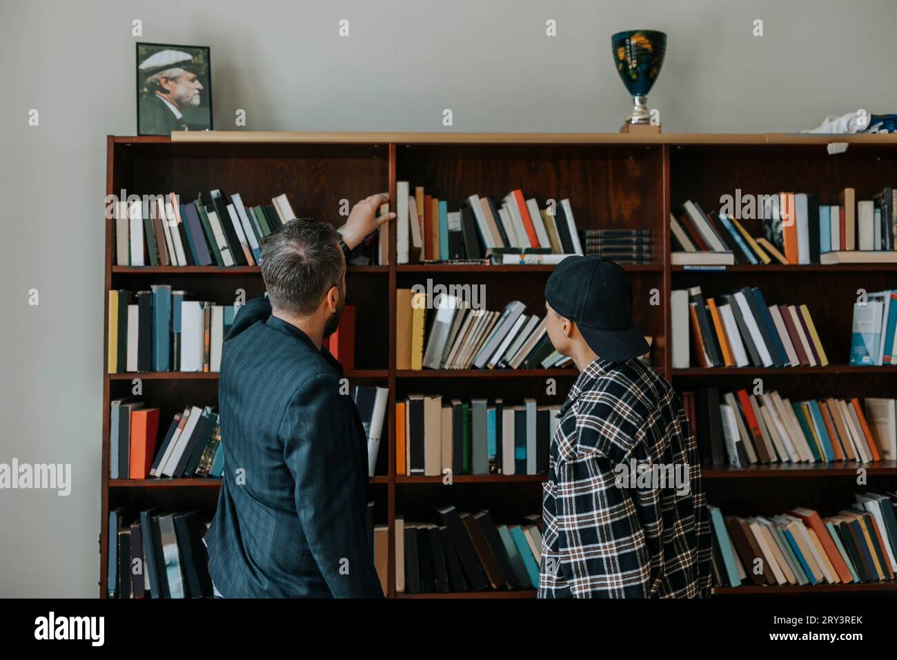 Professore maschio maturo che cerca di ottenere un libro mentre si trova da studente in biblioteca Foto Stock