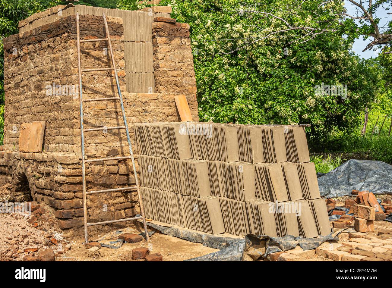 Zihuatanejo, Messico - 18 luglio 2023: Primo piano sullo storico forno di terracotta. Pila di piastrelle piatte essiccate pronte per essere caricate nel forno. Scala nelle vicinanze e verde Foto Stock