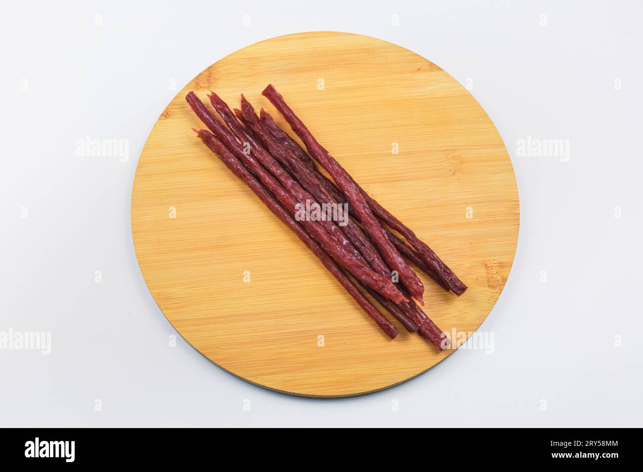 Deliziose salsicce di carne rossa secca. Salsicce sottili su un pannello di legno su sfondo bianco. Foto Stock