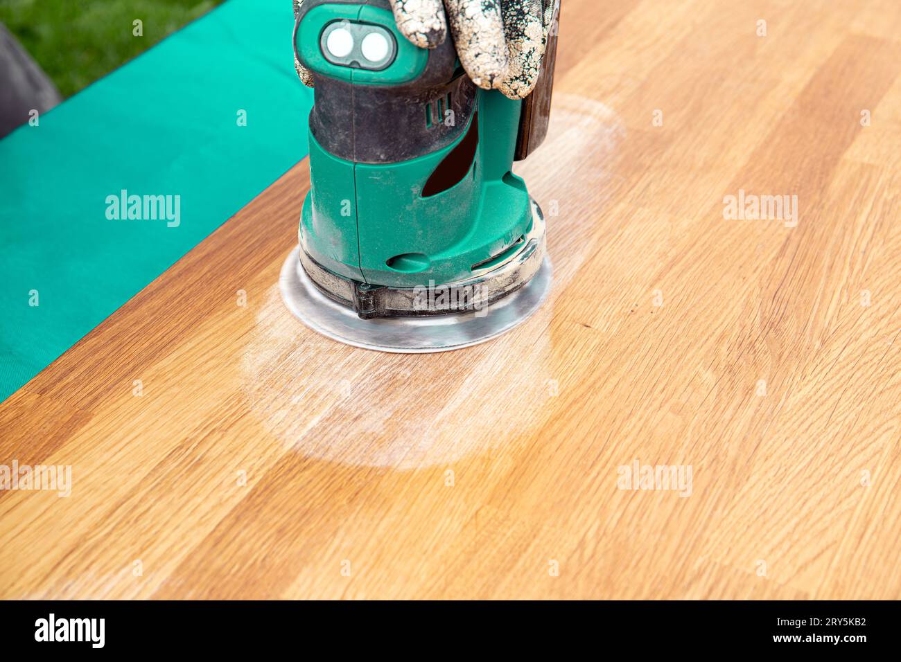 Vista ravvicinata della persona che lavora con la levigatrice, levigando le macchie sul vecchio blocco macellaio danneggiato su un tavolo di legno oliato. Concetto di ristrutturazione. Foto Stock