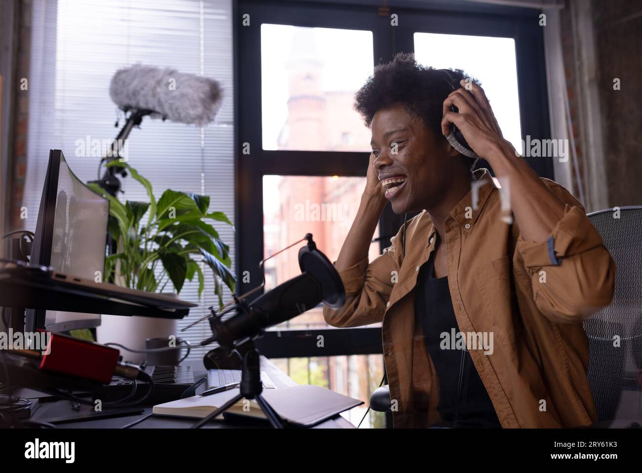 Felice uomo afro-americano con cuffie che realizza podcast dal vivo dalla scrivania di casa, spazio per le copie Foto Stock