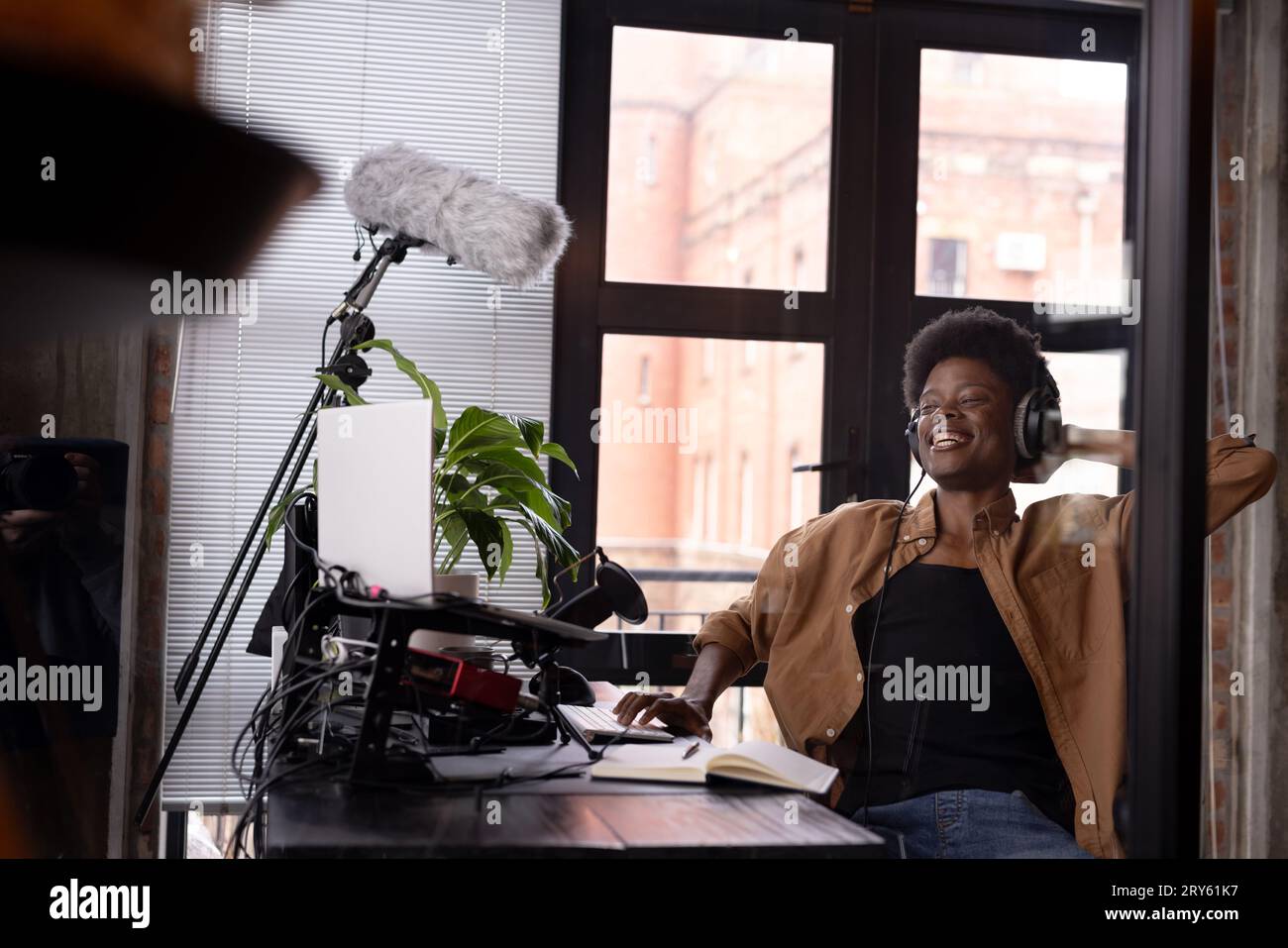 Felice uomo afro-americano con cuffie che realizza podcast dal vivo dalla scrivania di casa, spazio per le copie Foto Stock