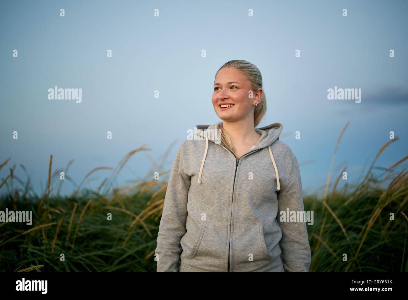 Donna sorridente in piedi contro il campo agricolo e ammirando la natura Foto Stock
