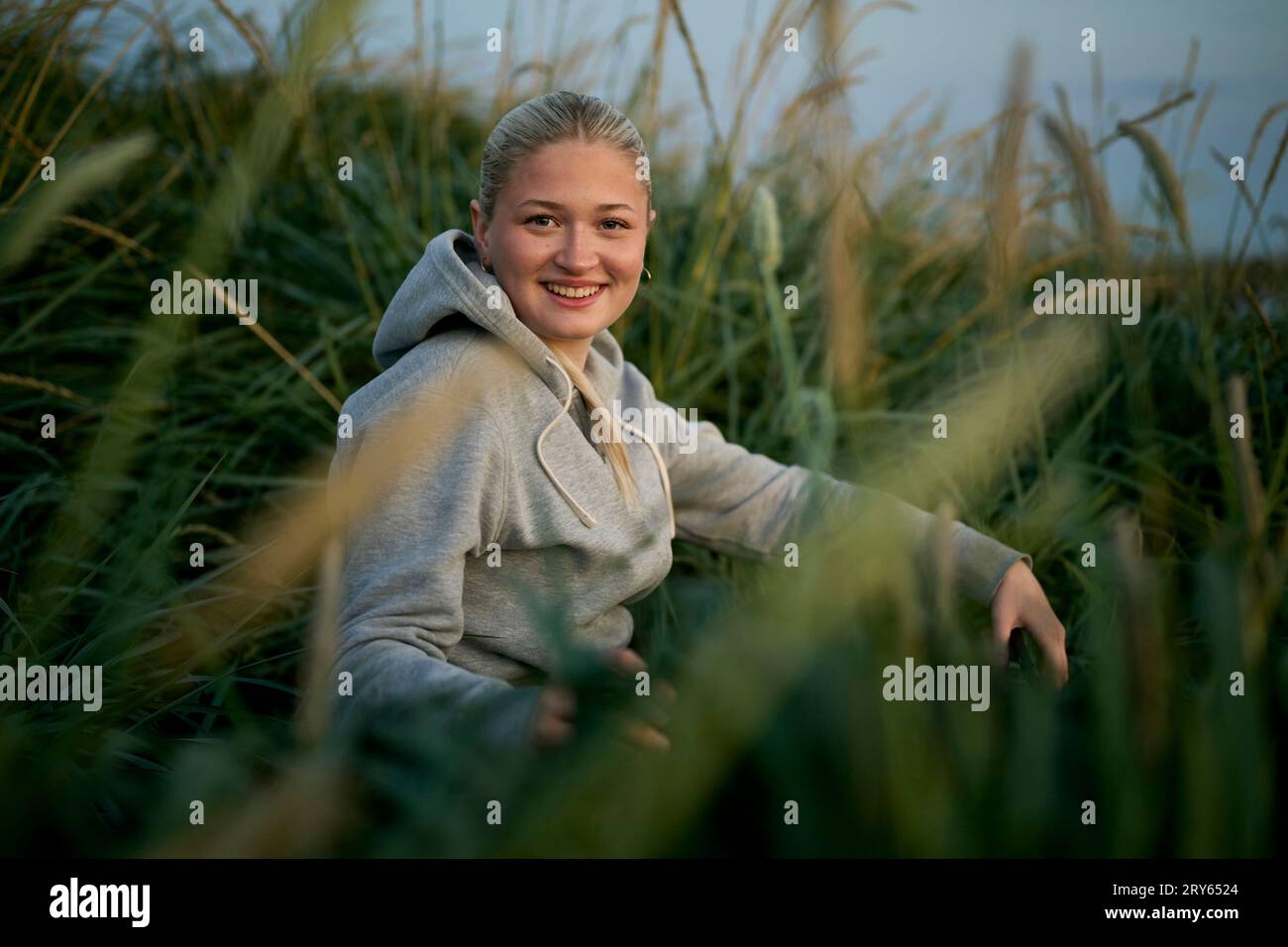 Donna sorridente seduta in mezzo a un'erba alta in un campo rurale Foto Stock