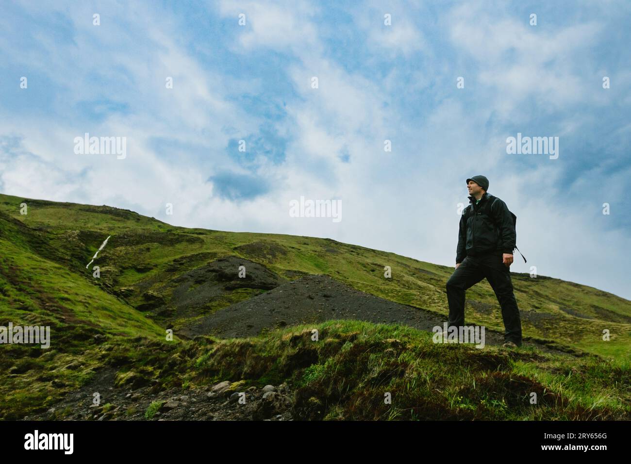 Uomo in cima a una montagna verde con cieli blu Foto Stock
