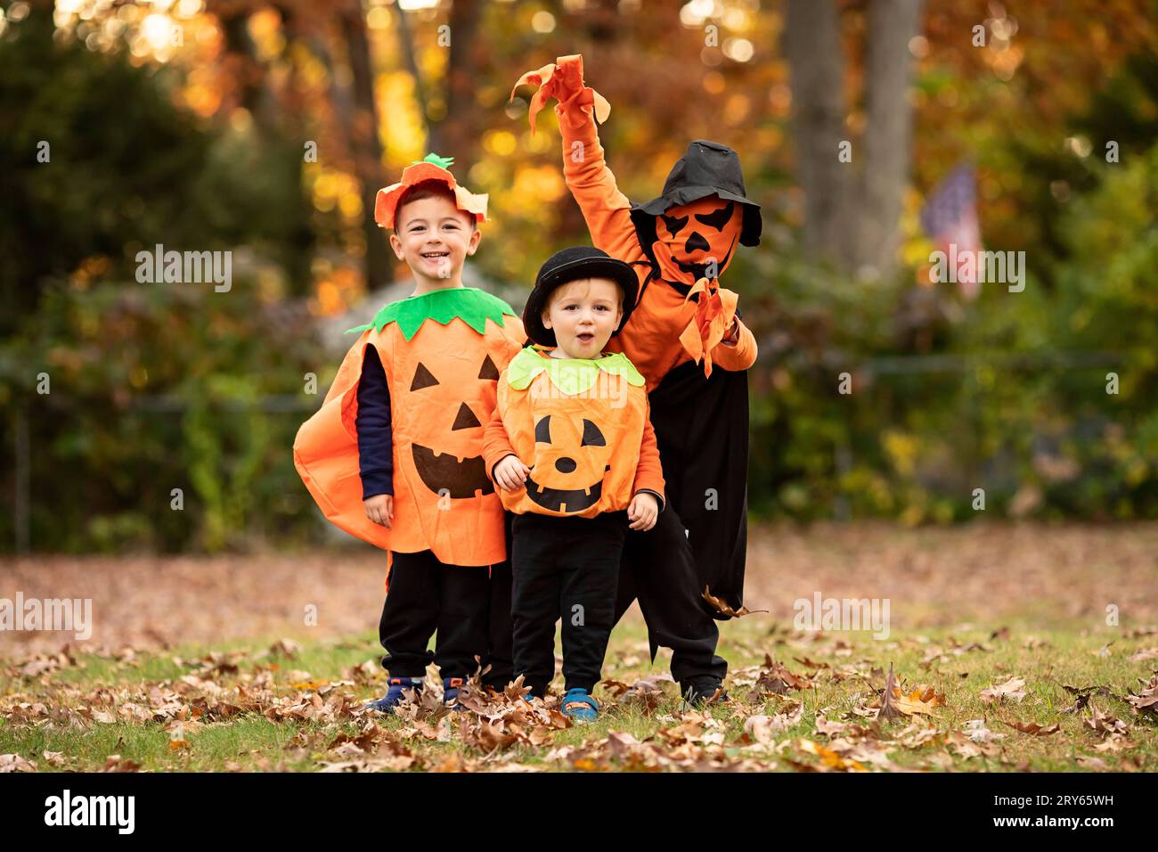 Tre ragazzini vestiti come zucche per halloween in cortile Foto Stock