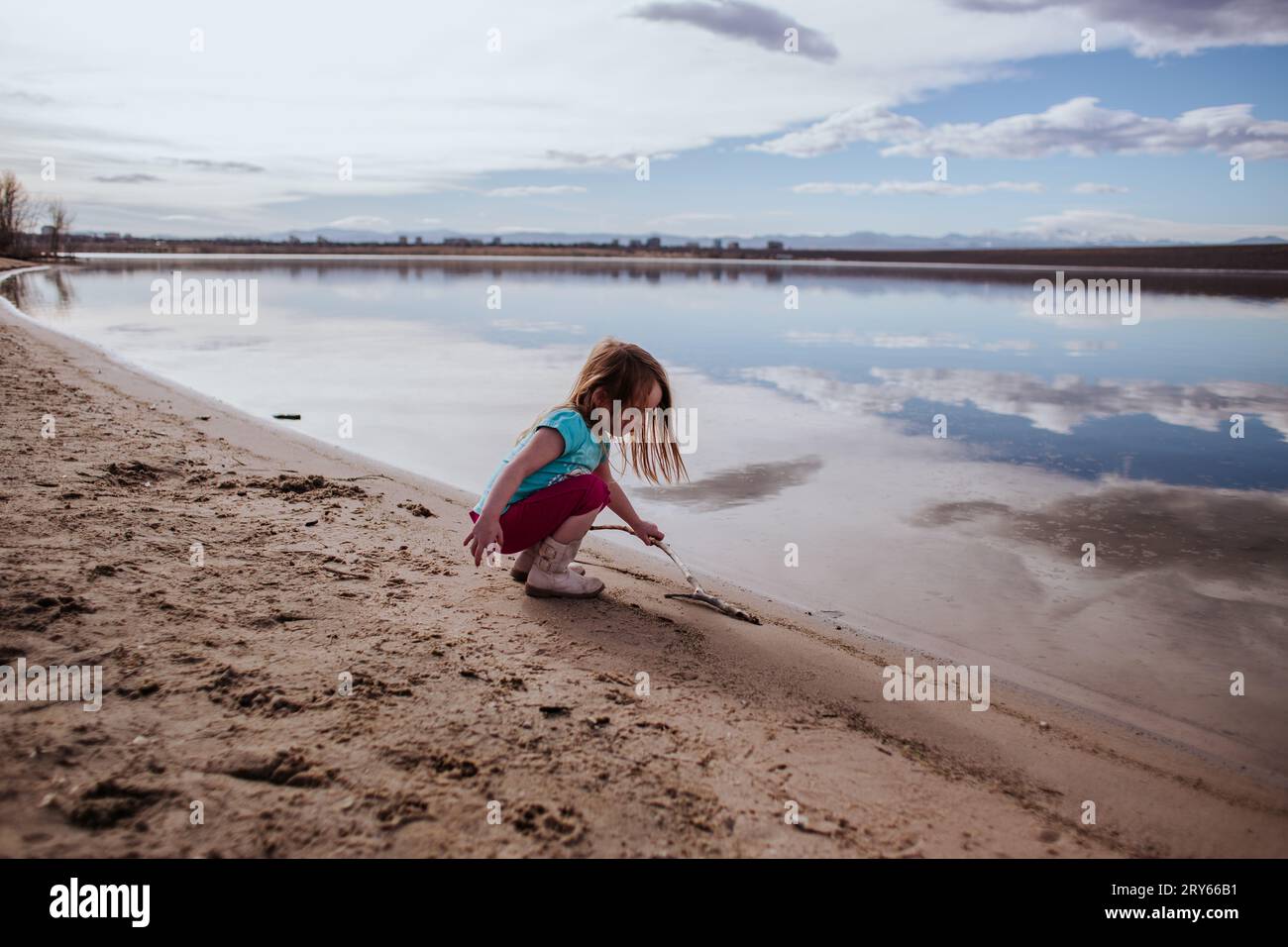 Giovane ragazza che gioca con il bastone sul bordo di Calm Lake Foto Stock