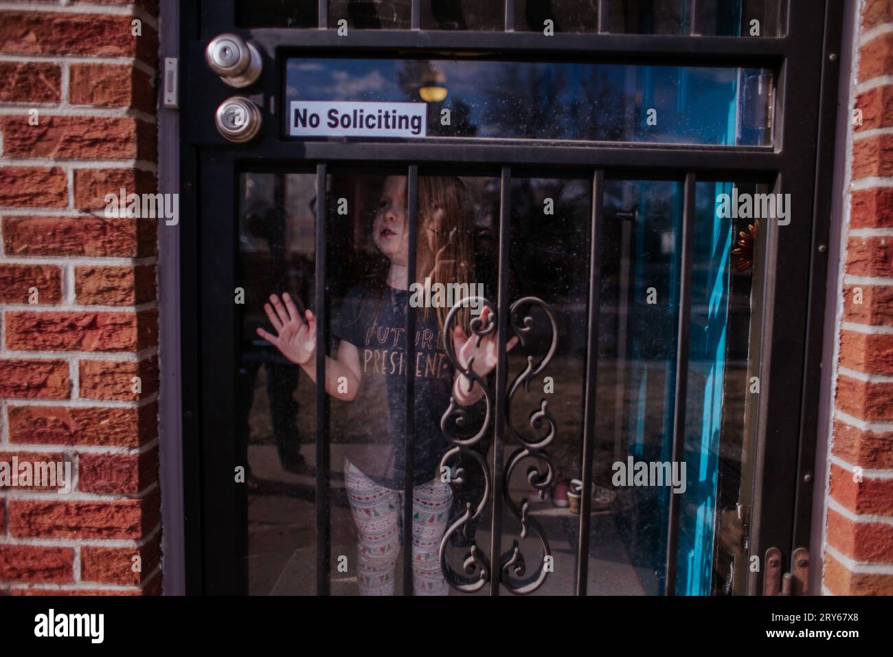 Triste bambina che guarda fuori dalla porta dello schermo Foto Stock