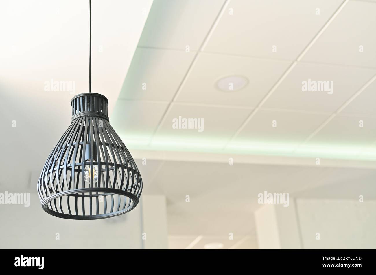 Una bella lampada su un lungo filo è appesa al soffitto. contro un muro bianco. Foto Stock