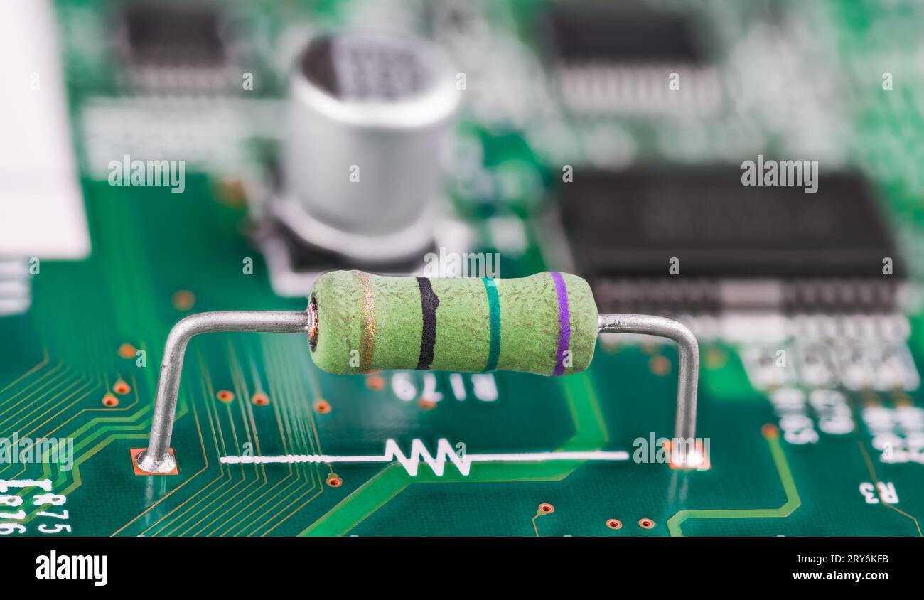 Primo piano di un resistore e del simbolo elettronico bianco sulla superficie verde del circuito stampato. Piccolo componente con codice colore e terminali con filo metallico sulla scheda a circuito stampato. Foto Stock