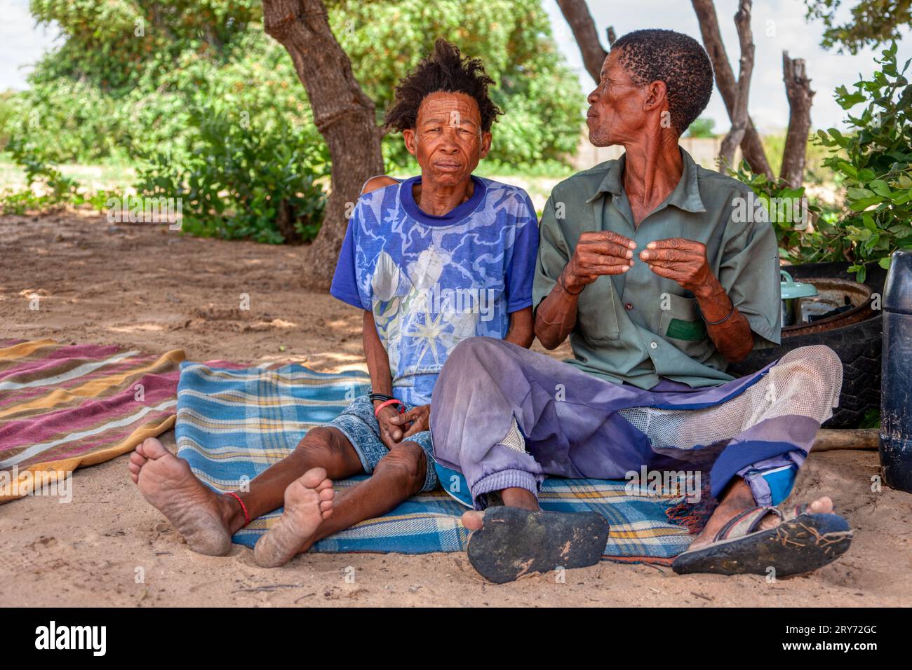 Un vecchio bushman san del Kalahari centrale, villaggio di New Xade in Botswana, di fronte al suo cortile seduto con la moglie Foto Stock