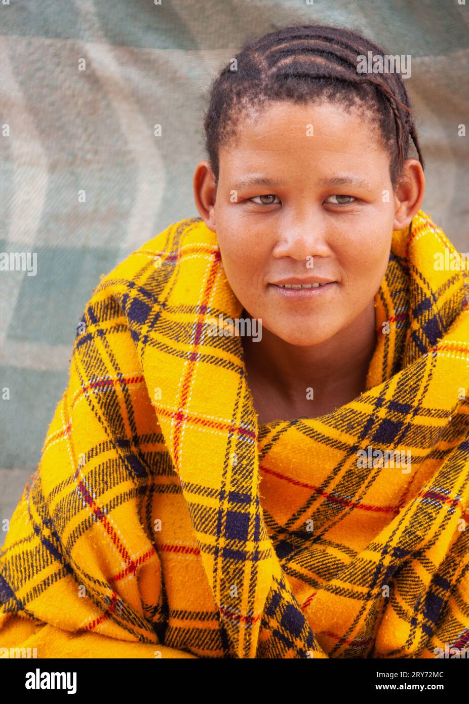 Una giovane donna di san boscimani del Kalahari centrale, villaggio di New Xade in Botswana, avvolta su una coperta gialla nel cortile della casa dopo il trasferimento Foto Stock