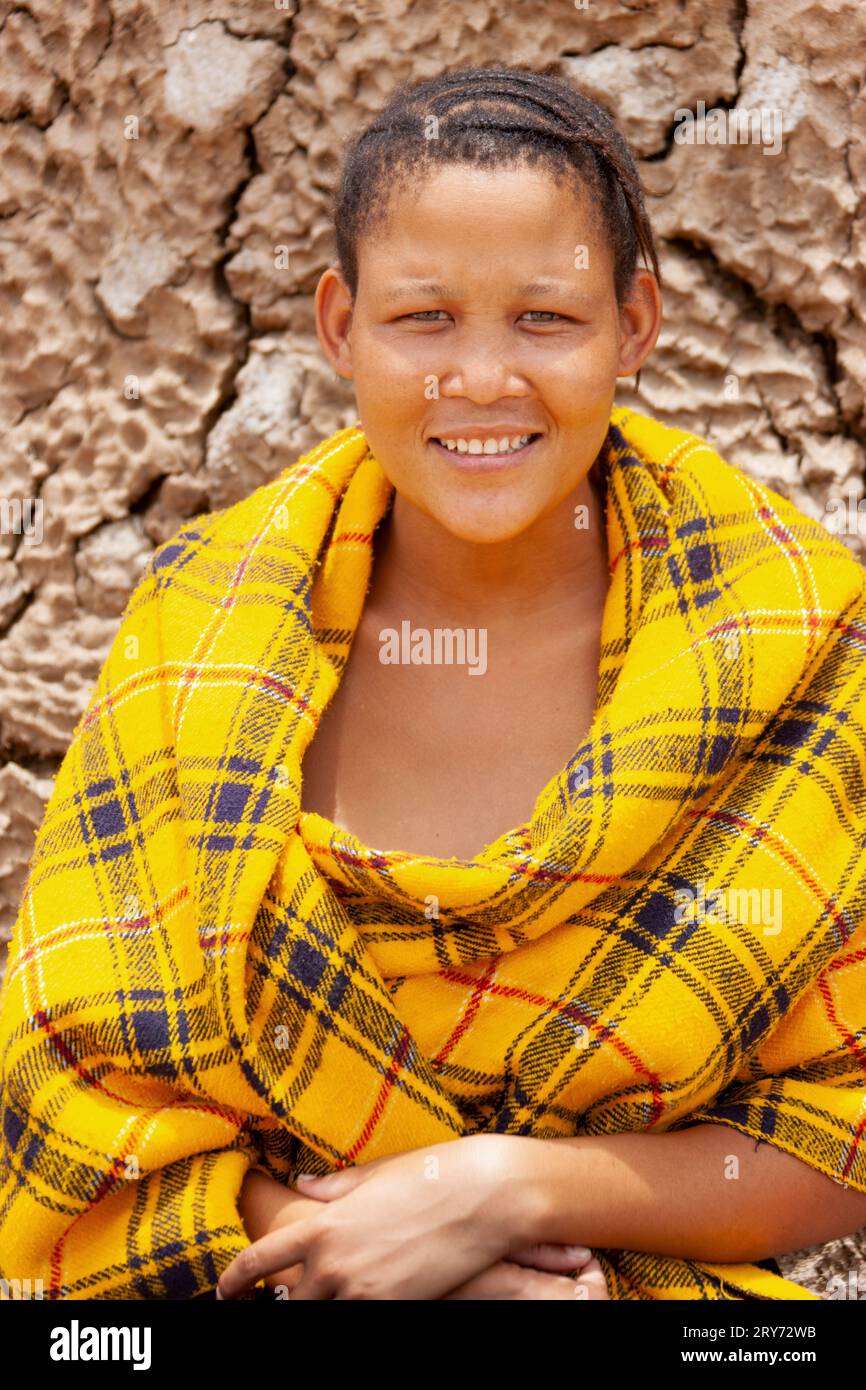 Una giovane donna di san boscimani del Kalahari centrale, villaggio di New Xade in Botswana, avvolta su una coperta gialla nel cortile della casa dopo il trasferimento Foto Stock