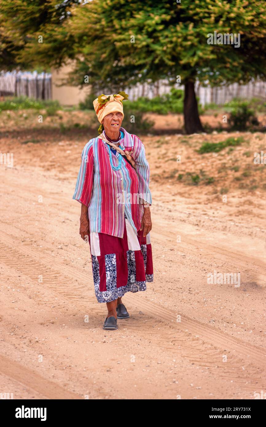 vecchia donna africana basarwa che cammina su una strada sterrata nel villaggio tradizionale Foto Stock