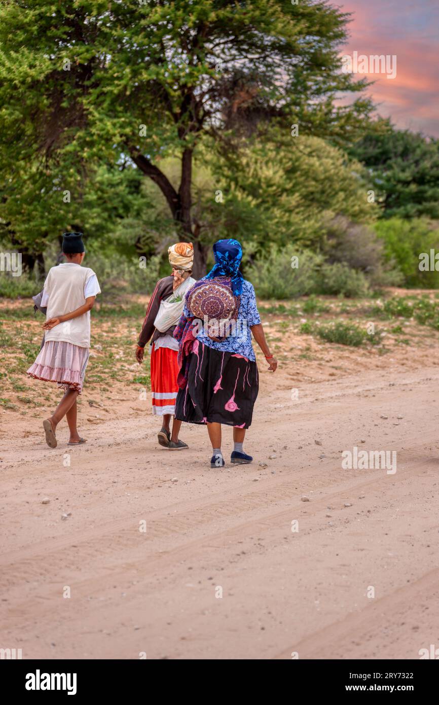 tre donne africane basarwa passeggiano su una strada sterrata per raggiungere il villaggio tradizionale Foto Stock