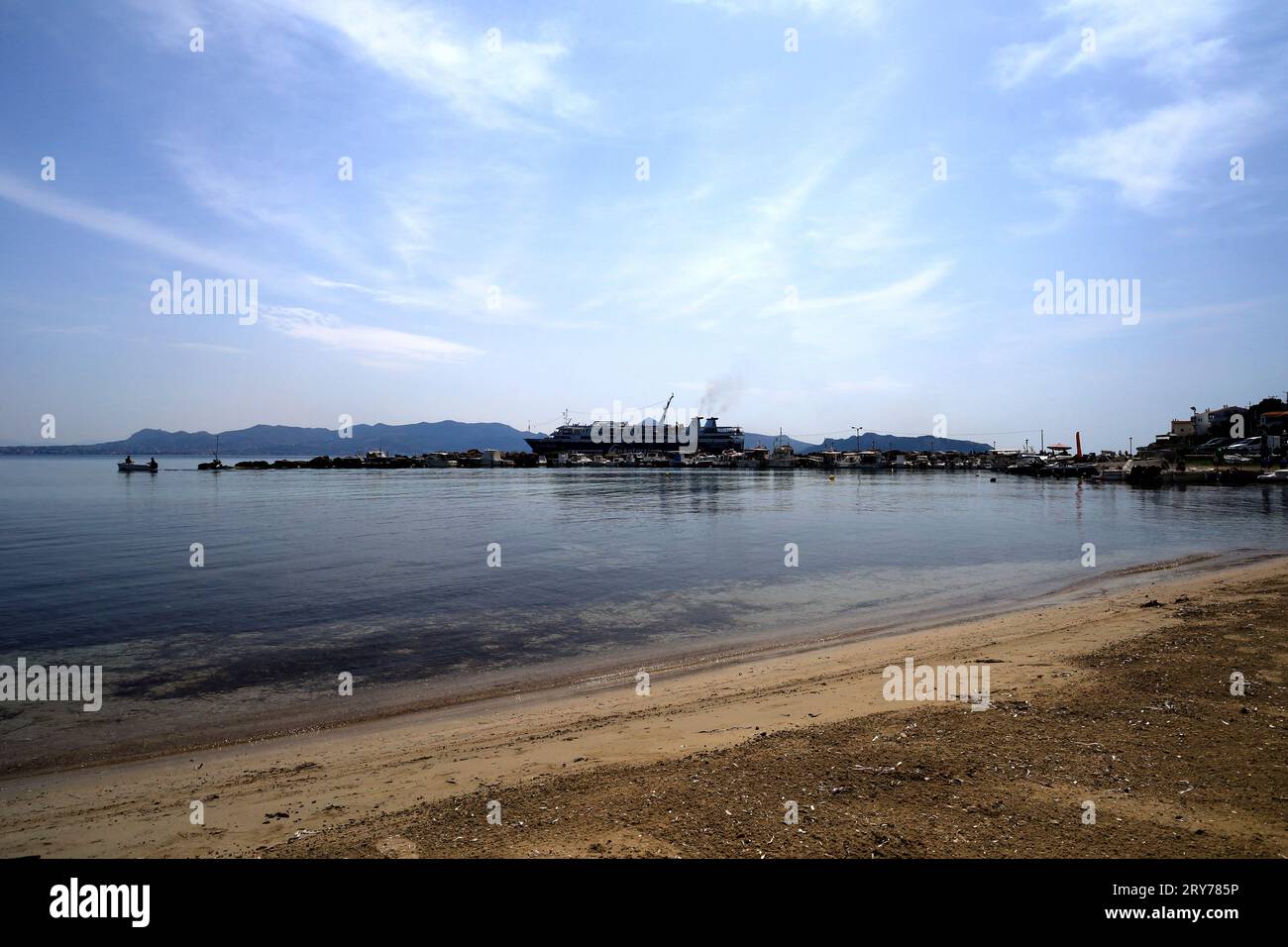 Traghetto al porto di Skala e piccolo peschereccio al largo del frangiflutti, Agistri, gruppo delle isole Saroniche, Grecia. Mare calmo e cielo blu. Presa nel luglio 2023 Foto Stock