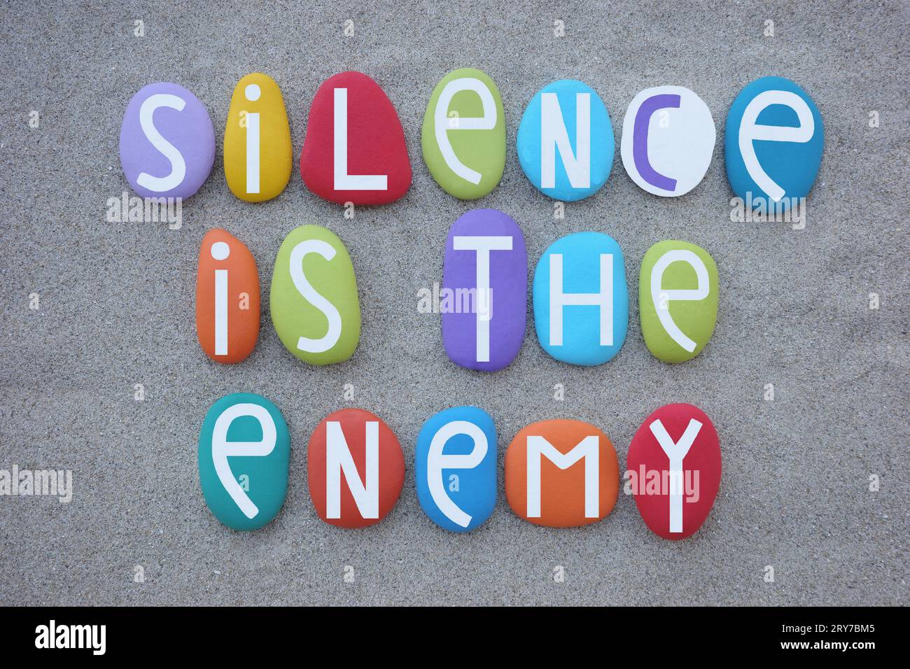 Silence è il nemico, slogan creativo composto da lettere di pietra multicolore sulla sabbia della spiaggia Foto Stock
