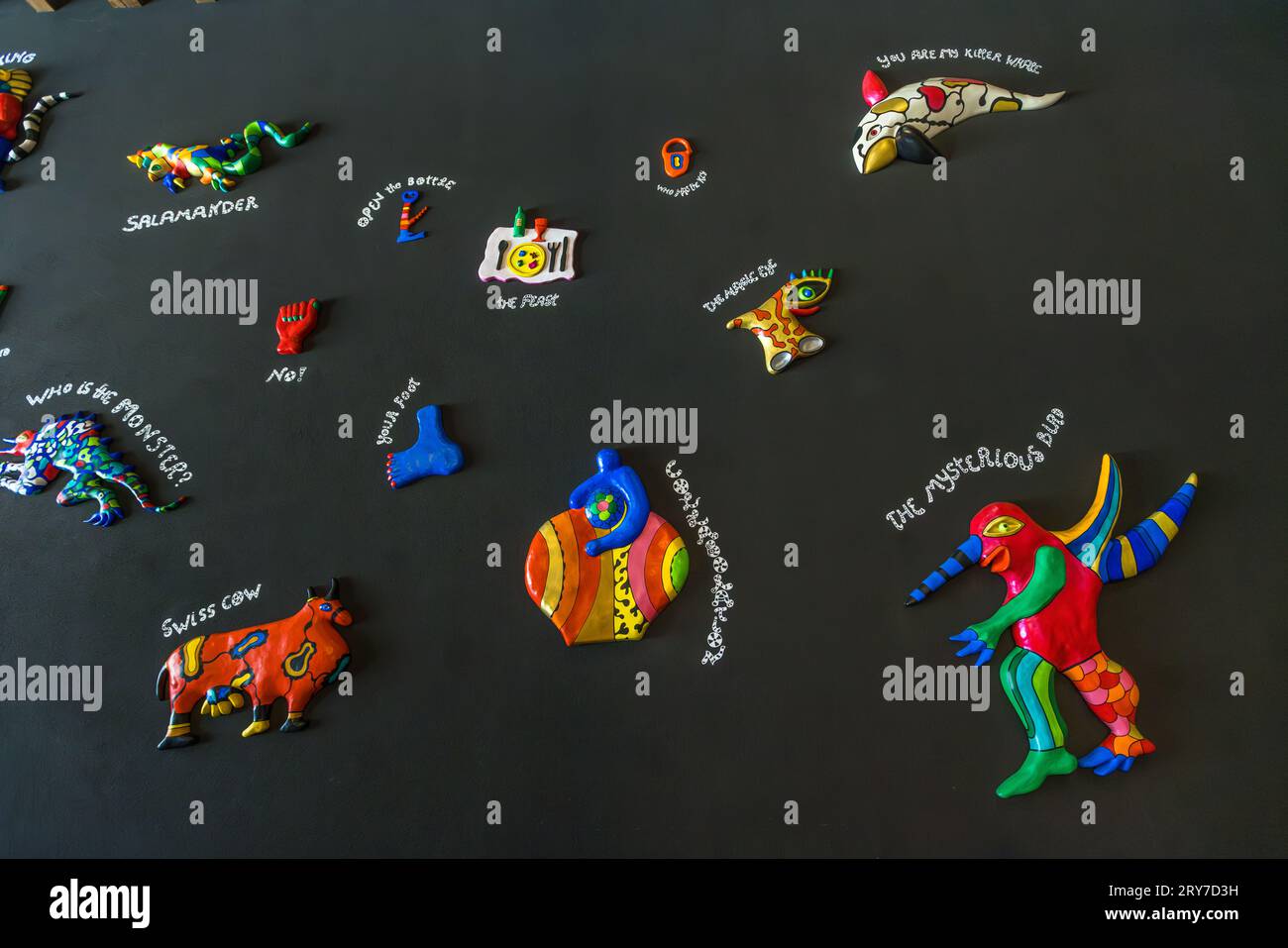 Piccoli rilievi laccati di colore brillante della serie "Remembering" (1997/98) di Niki de Saint Phalle sono appesi a un muro scuro presso l'Espace Jean Tinguely – Niki de Saint Phalle a Friburgo, in Svizzera. Titoli scritti a mano come "Salamandra", "Mucca svizzera", "L'uccello misterioso" e "Tu sei il mio orca" accompagnano le singole figure. Ospitato dal 1998 in un ex deposito dei tram di Friburgo costruito nel 1900, il museo espone anche l'opera chiave di Jean Tinguely "Retable de l'Abondance occidentale et du Mercantilisme totalitaire" (1989/90). Foto Stock