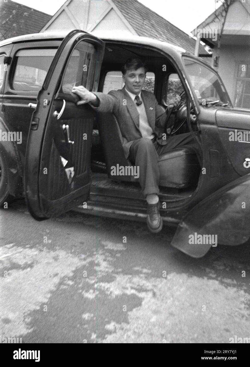 Anni '1960, storici, parcheggiati fuori chalet in un campo di vacanze, un giovane in auto dell'epoca, con porte che si aprono verso l'esterno, incernierate nel mezzo dell'auto, Inghilterra, Regno Unito. Tali porte sono anche note come porte suicidi, in quanto potrebbero essere pericolose se aperte quando la vettura era in movimento. Foto Stock