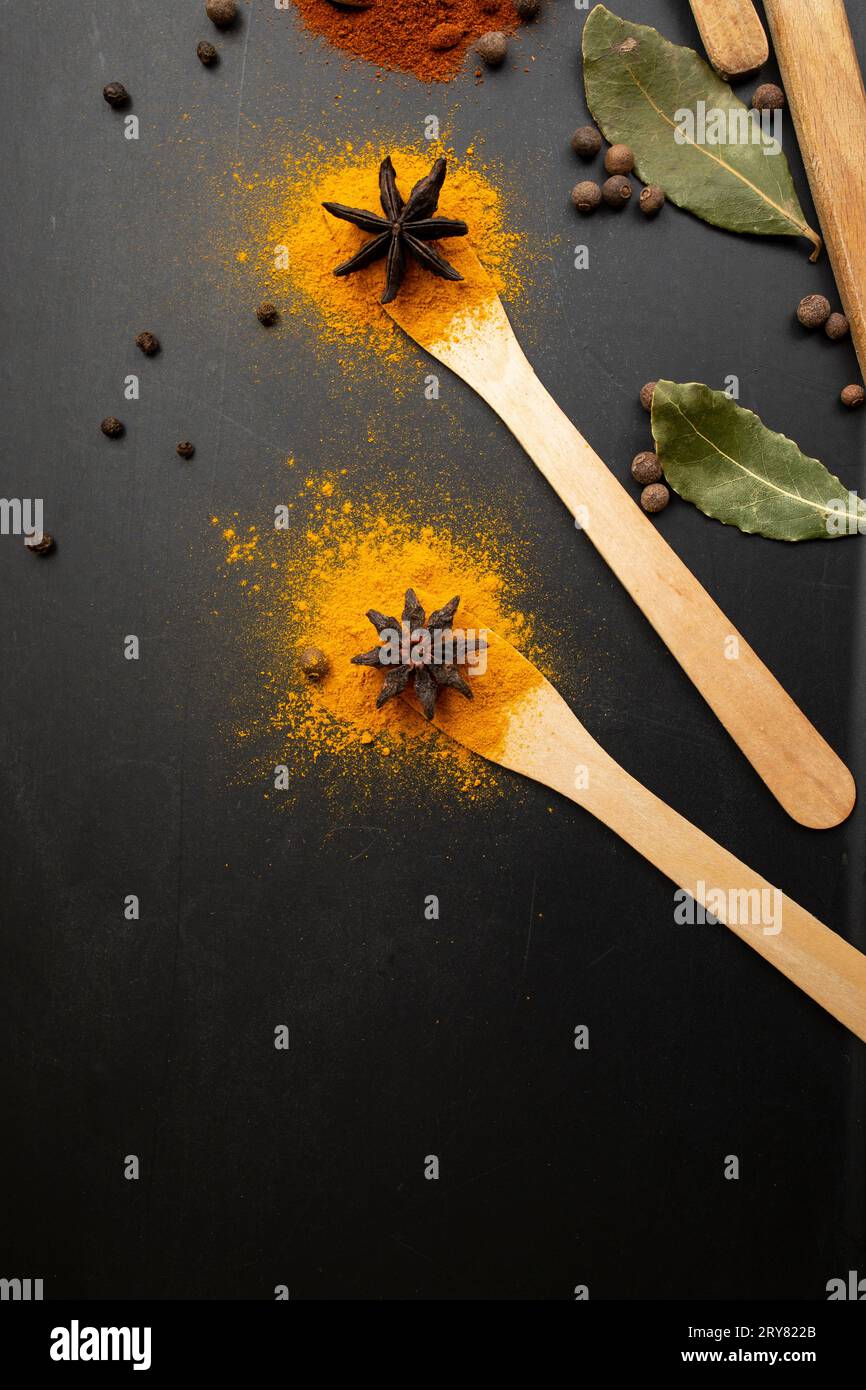 Paprika, curcuma e foglie di alloro disposte come fiori su cucchiai da tè in legno su sfondo nero Foto Stock