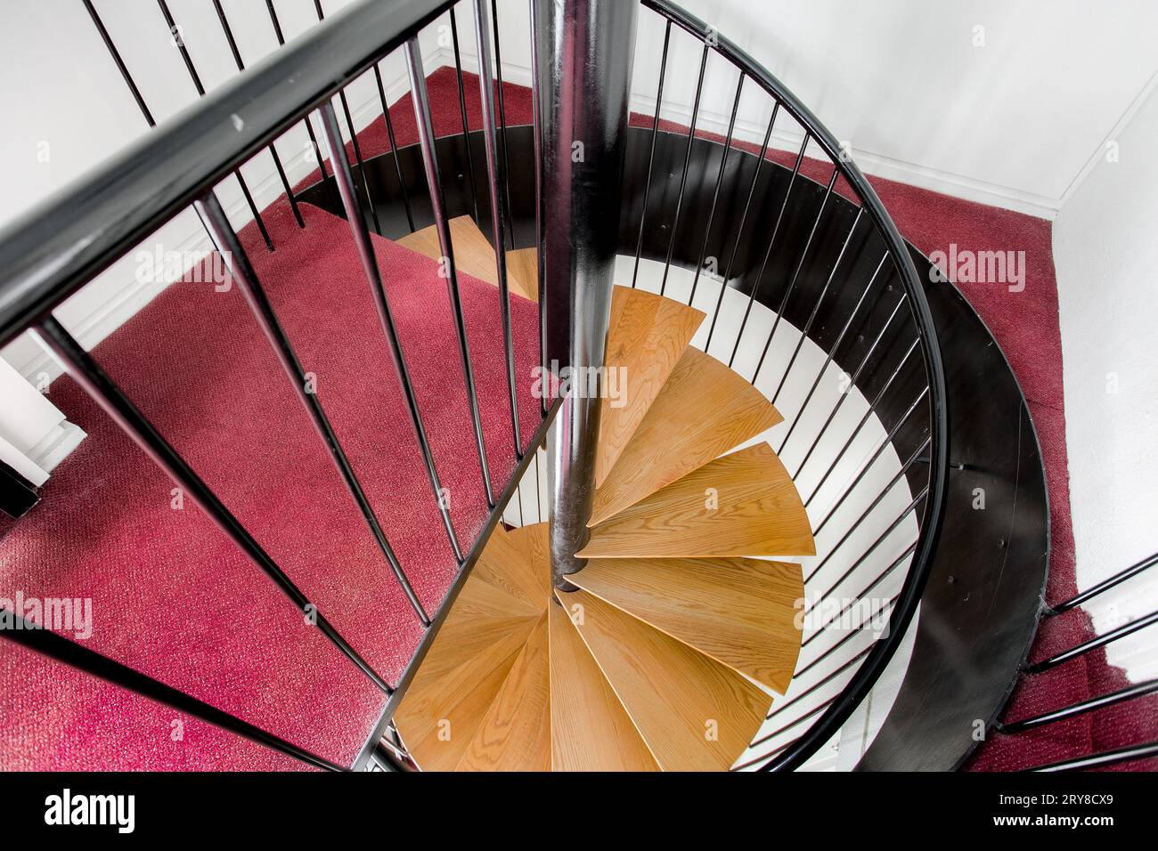 Scala a spirale con guida nera con scale in legno e moquette Borgogna e interno bianco Foto Stock