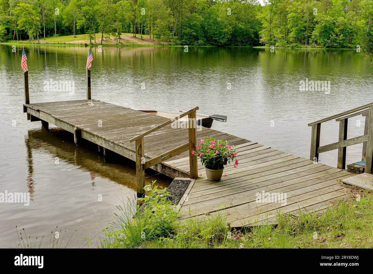 Molo rilassante con vaso di fiori e Bandiere americane su pali di legno sul lago in estate Foto Stock