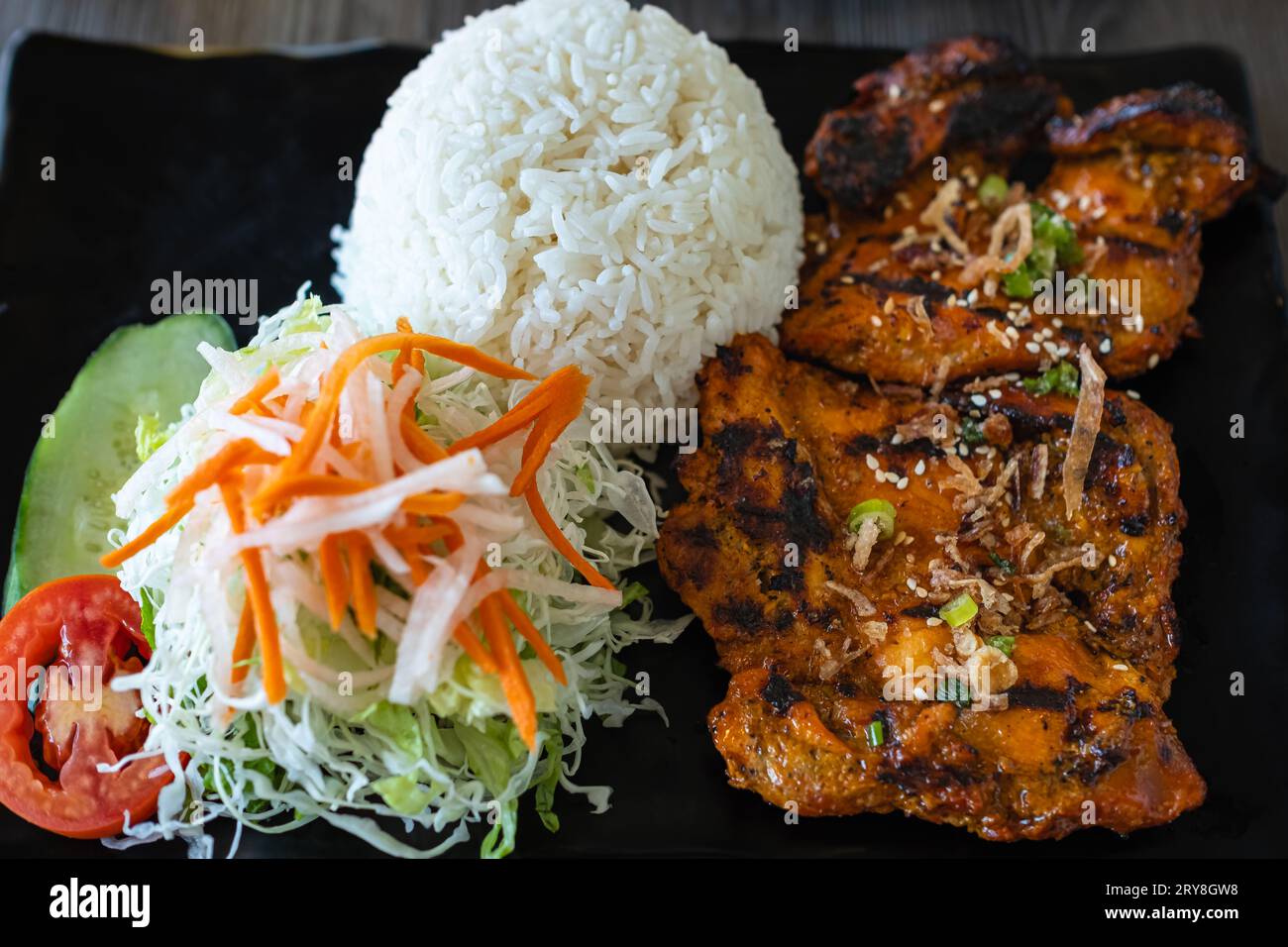 Pollo alla griglia con riso e insalata di cavolo rosso su sfondo nero. Primo piano di riso di pollo in stile asiatico. Cibo in stile asiatico. Pollo alla griglia tailandese. Foto Stock