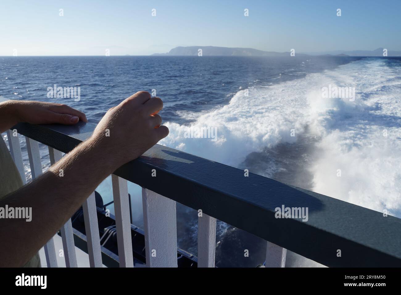 Ringhiere della nave con due mani appoggiate su di essa. Sullo sfondo c'è l'acqua di chiglia. Foto Stock