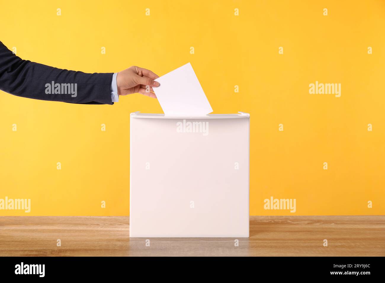 Donna che mette il suo voto nelle urne su un tavolo di legno su sfondo arancione, primo piano Foto Stock