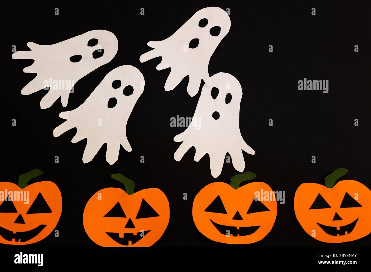 fantasmi di carta che volano sulle zucche su uno sfondo nero, concetto di halloween con artigianato e decorazioni Foto Stock