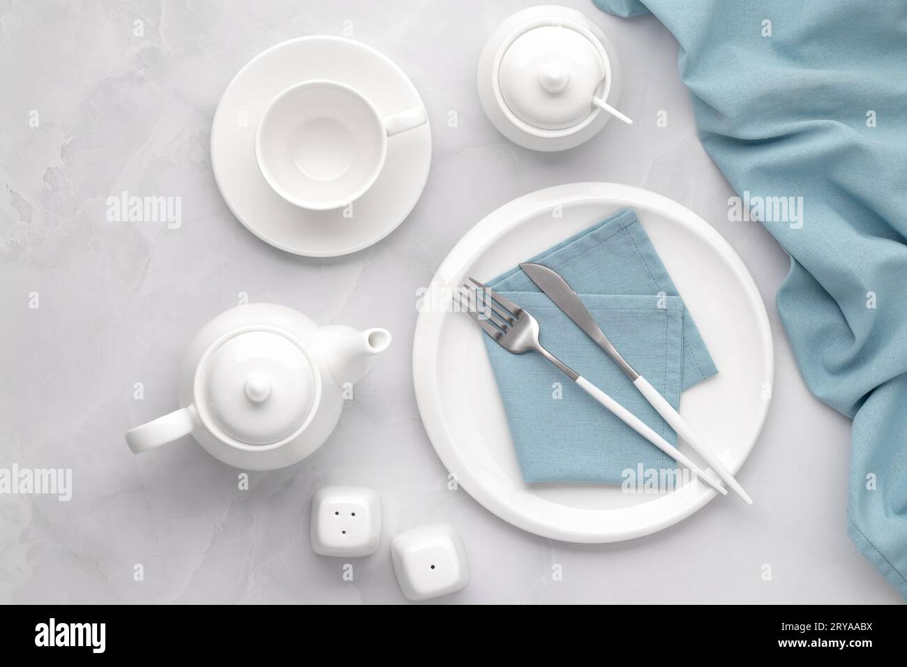 Stoviglie e posate in ceramica bianca. Stoviglie, stoviglie, teiera e tazza su fondo in marmo grigio, tavolo con piatto vuoto, forchetta e k Foto Stock